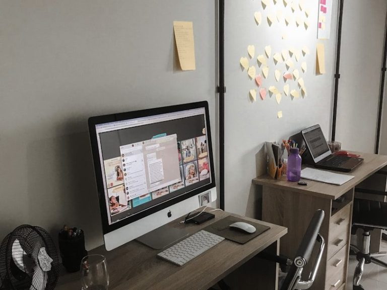 A workspace featuring an iMac, a laptop, and a wall covered in sticky notes.