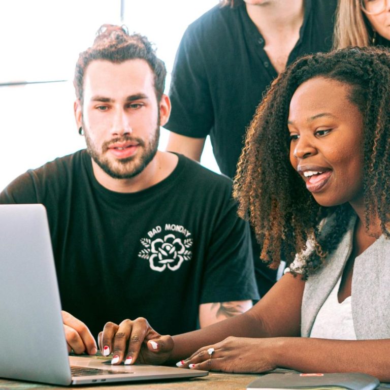 A diverse group of young people collaboratively working on a laptop.