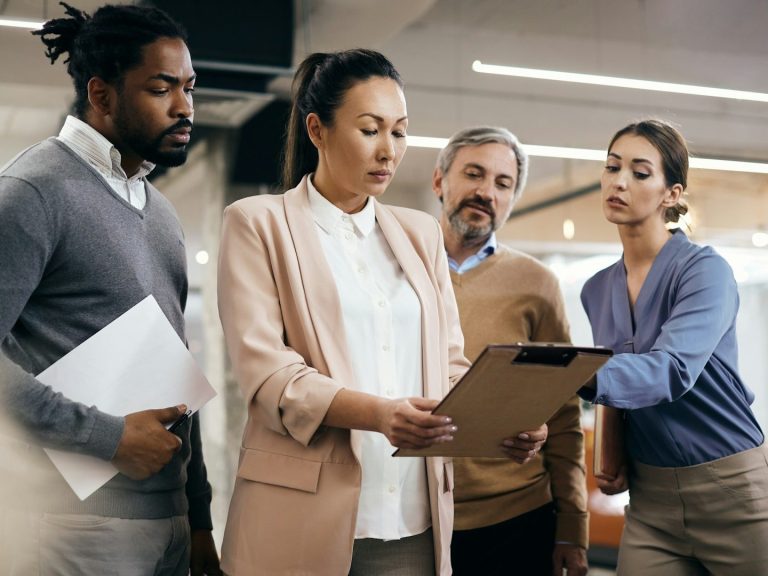 Four colleagues discussing work while reviewing documents in a modern office setting.