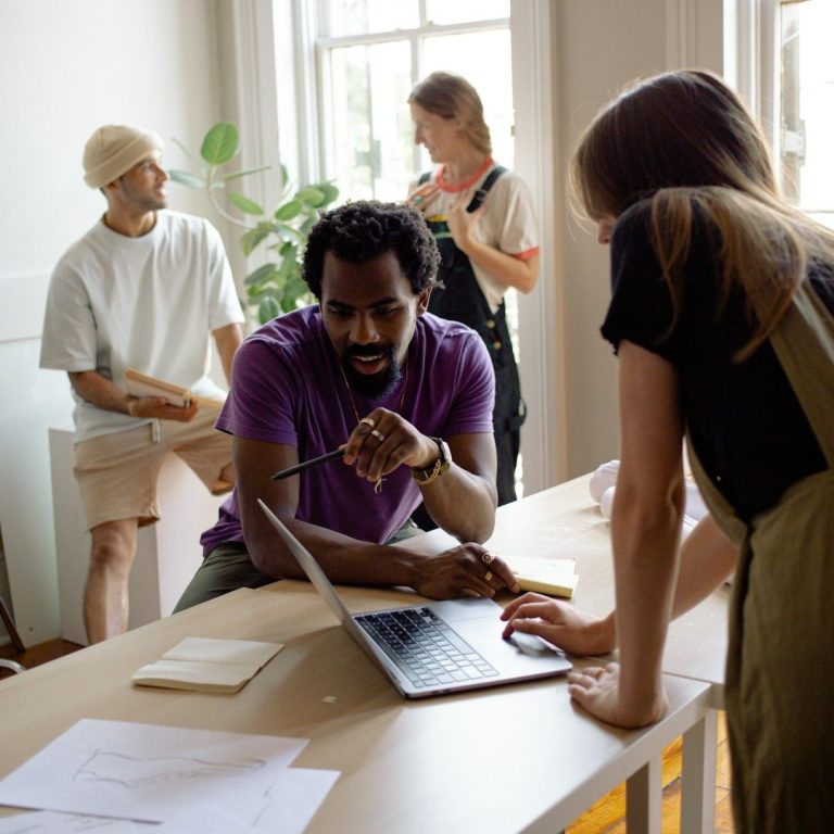 A group of four people collaborating around a table with a laptop and notepad.