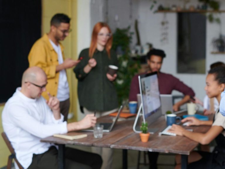 A diverse group of professionals collaborating around a table with laptops and notebooks.