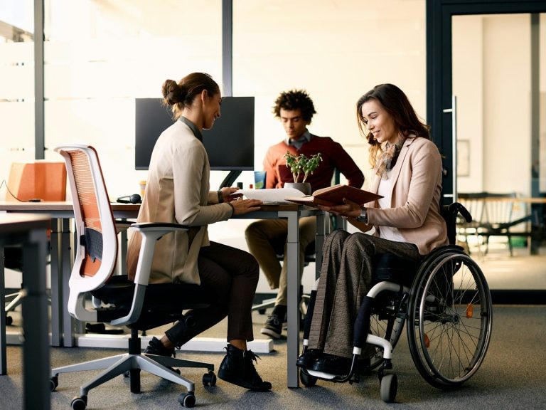 Three people in an office setting, one in a wheelchair, discussing over documents.